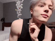 a man wearing a black tank top and a silver necklace looks at the camera