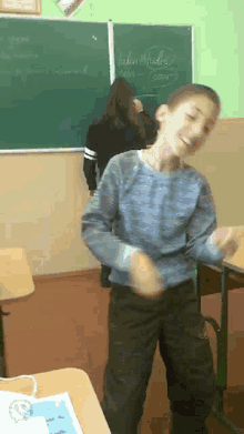 a boy in a blue shirt is dancing in front of a blackboard that says " helen " on it
