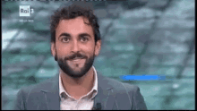 a man with a beard and a suit is smiling on a television show .
