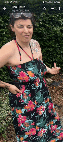 a woman in a floral dress is standing in front of a hedge with the time of 19:33