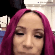 a close up of a woman with pink hair making a face .