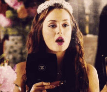 a woman with a tiara on her head is holding a chanel makeup palette