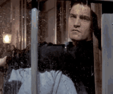 a man is looking out of a window with water drops on it