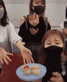 a group of people wearing face masks are standing around a plate of food