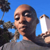 a close up of a woman 's face with a shaved head and a blue sky in the background .