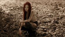 a woman with red hair is kneeling in a muddy field