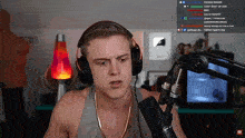a man wearing headphones and a gold chain stands in front of a microphone on a twitch stream