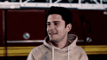 a man wearing a tan hoodie is smiling in front of a red fire truck