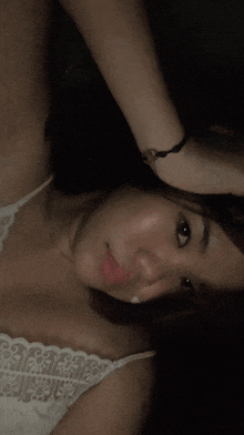 a woman laying down with her hand on her head wearing a white lace top