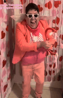 a man in a pink suit and white sunglasses is standing in front of a wall with hearts on it