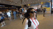 a woman wearing sunglasses and a lanyard around her neck walks through a crowded area