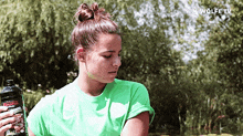 a woman in a green shirt holds a bottle of water