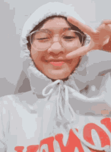a girl wearing glasses and a white hoodie with the word amo on it giving a peace sign