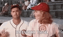 a man and a woman are standing next to each other on a baseball field . the woman is wearing a red hat .