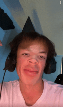 a young man wearing headphones and a white shirt looks at the camera
