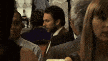 a man in a suit and tie is sitting in a crowded room .