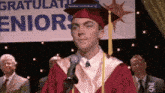 a man in a graduation cap and gown stands in front of a sign that says congratulations eniors