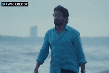 a man wearing glasses and a blue shirt is standing on a beach with a twitter logo above him that says 7wickreddy