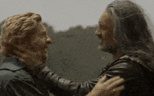 two men with long hair are hugging each other in a field