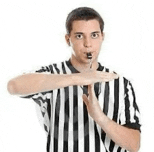 a man in a striped shirt is holding a whistle in his mouth and making a stop sign .