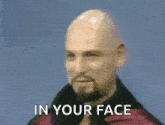 a bald man with a beard and a ring on his finger is making a devil horns sign with his hands .