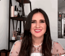 a woman with long dark hair is smiling in front of a shelf in a room .