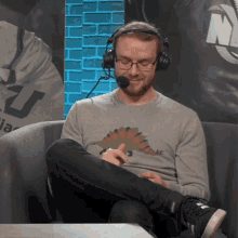 a man wearing headphones and a dinosaur shirt sits on a chair