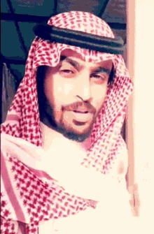 a man with a beard is wearing a red and white checkered head scarf .