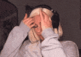 a woman wearing headphones is holding her head in pain