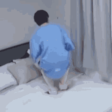 a man in a blue shirt is kneeling on a bed with his legs crossed .