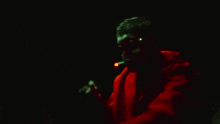 a man wearing sunglasses is smoking a cigarette in a dark room