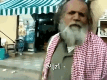 a man with a beard and a plaid shirt is standing in front of a store .