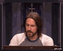 a man with long hair and a beard is sitting in front of a screen with gifs.com written on it