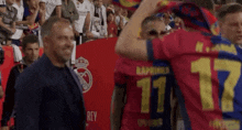 a man in a suit is standing next to a man in a red shirt with the number 11 on it .