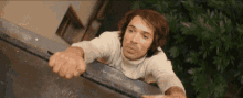 a man in a white sweater is leaning over a metal fence .