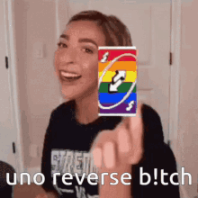 a woman is holding a rainbow uno card in front of her face and says uno reverse bitch .