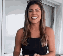 a woman wearing sunglasses and a black tank top is smiling and looking at the camera .