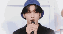a young man wearing a blue hat is holding a microphone and making a heart shape with his fingers .