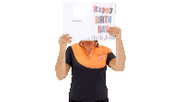 a woman in an orange shirt is holding up a happy birthday card in front of her face
