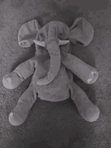 a stuffed elephant is laying on its back on a gray blanket