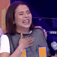 a woman is laughing and crying while holding a microphone in front of her chest .