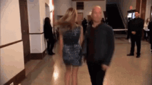 a man and a woman are walking down a hallway holding hands . the woman is wearing a blue dress .
