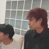 a man with red hair is sitting on a couch next to another man