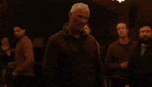 a man in a brown jacket stands in a dark room with christmas lights hanging from the ceiling behind him