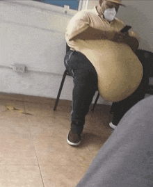 a man wearing a mask and a hat is sitting in a chair with a large belly .