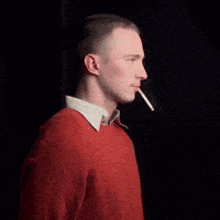 a man in a red sweater is smoking a cigarette in a dark room
