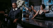 a man wearing headphones is standing at a bar while a woman pours a drink .