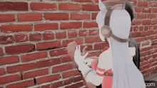 a woman is standing in front of a brick wall holding a brick .