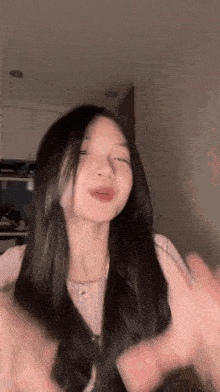 a young girl with long black hair is making a funny face while waving her hands in a room .