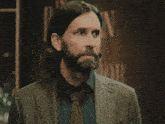 a man with a beard wearing a suit and tie is standing in front of a sign .